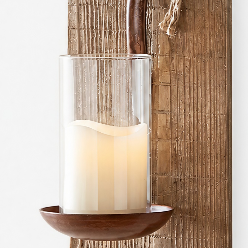 Close detail of glass shade, candle, iron cup, and textured wood backplate